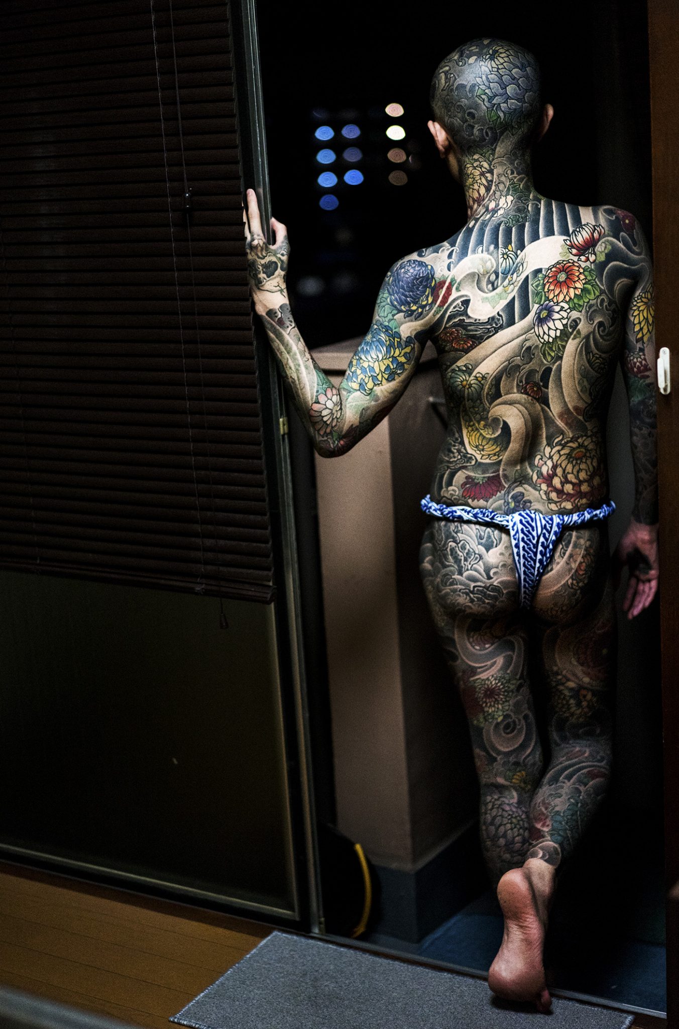 An apprentice of a traditional Japanese tattoo artist wearing traditional undergarment looking down from the balcony of a apartment in Tokyo