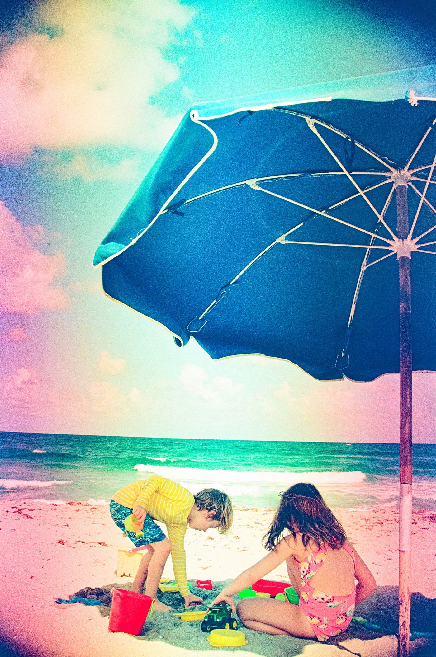 dreamy image of children playing in the sand under a beach umbrella at the ocean, "film soup" technique on 35mm film