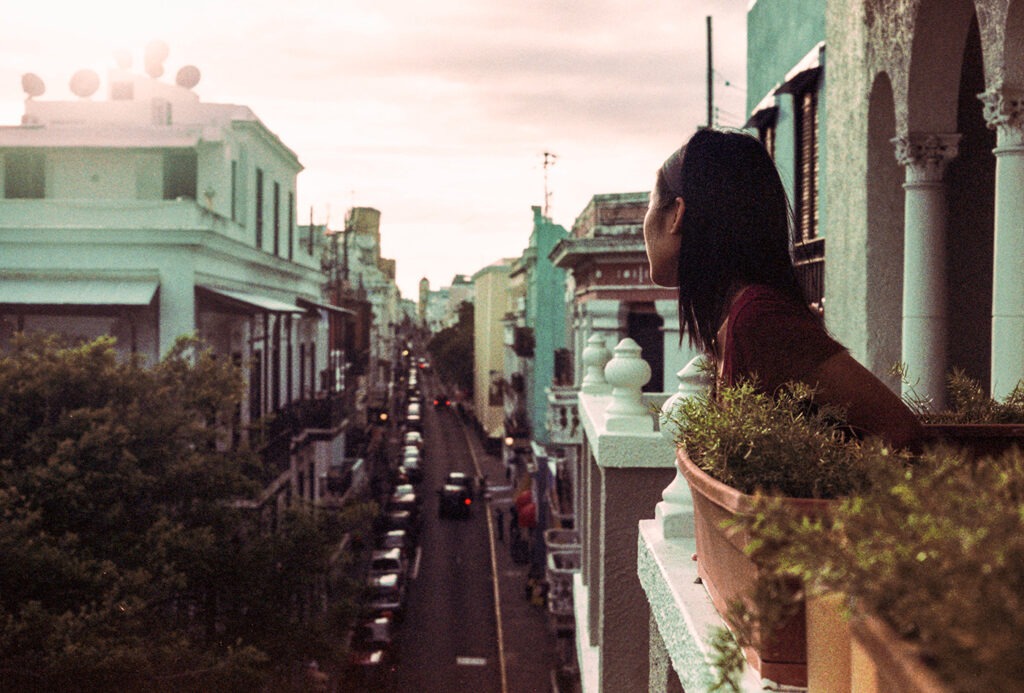 Girl Looking Out On A Balcony Over City Streets At Sunset Taken on a Canon AE-1 with Agfa CT Precisa in San Juan, Puerto Rico