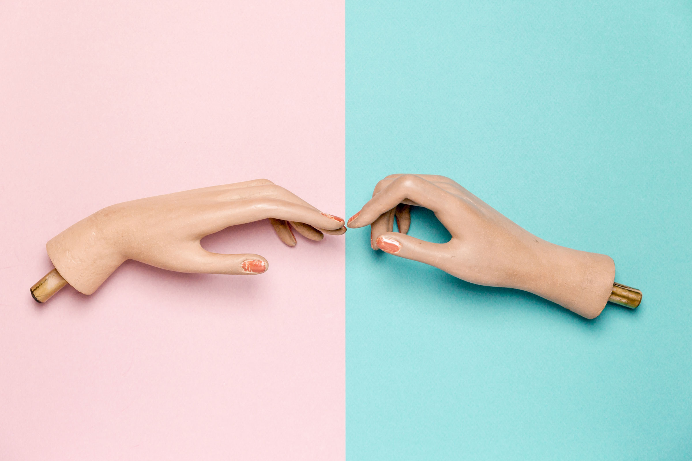Two plastic hands trying to connect together, blue and pink background