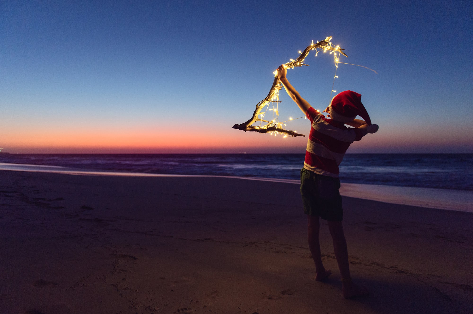Boy With Christmas Lights At The Beach After Sunset An evening at the beach at Christmas time in https://www.stocksy.com/angelalumsden/showcase?page=1 Australia