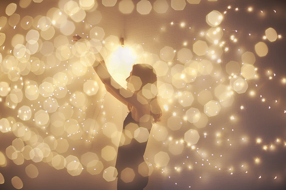 Double exposure shot of silhouette of a woman surrounded with lights. She decorates wall with led light garland. Warm color tone.