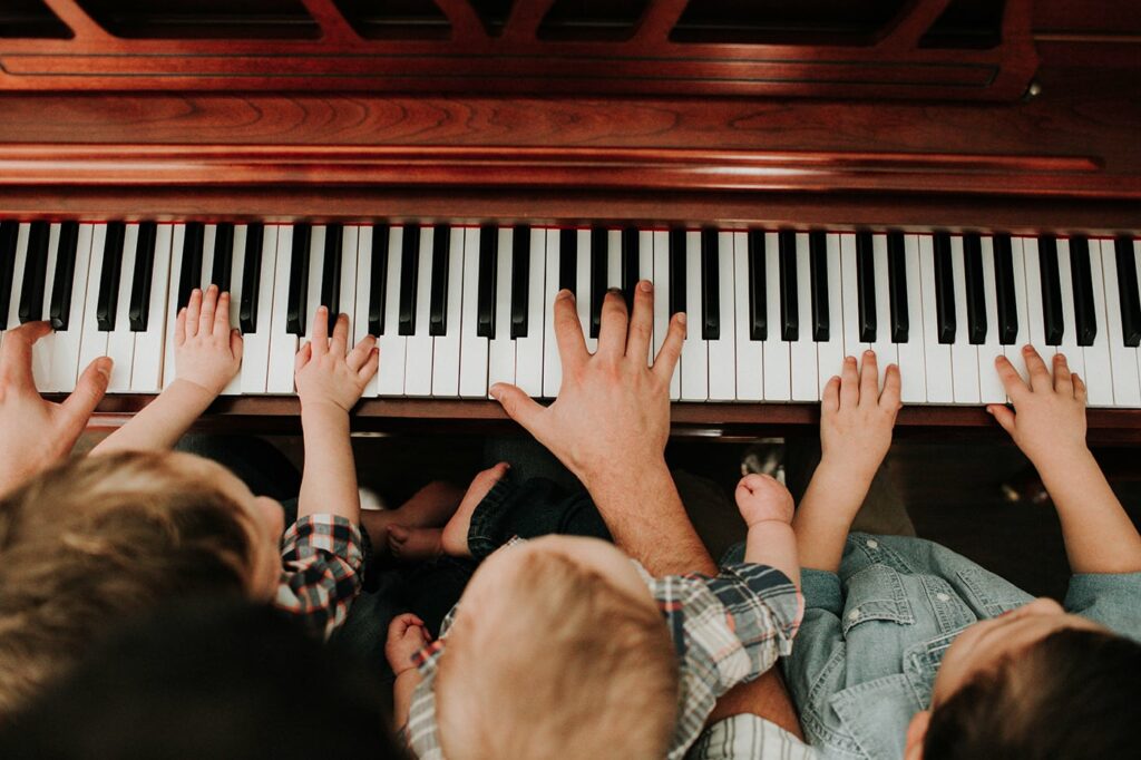 This is an image of a piano with the hands of a father and his sons on the keys