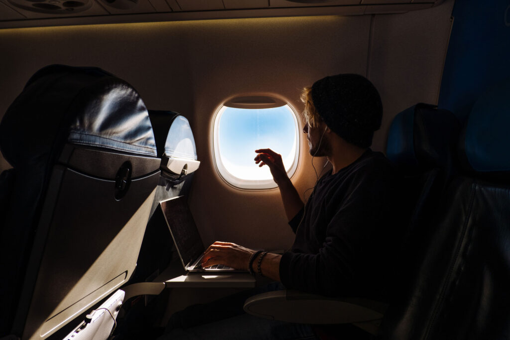 Young Man Working On A Laptop While Traveling In An Airplane