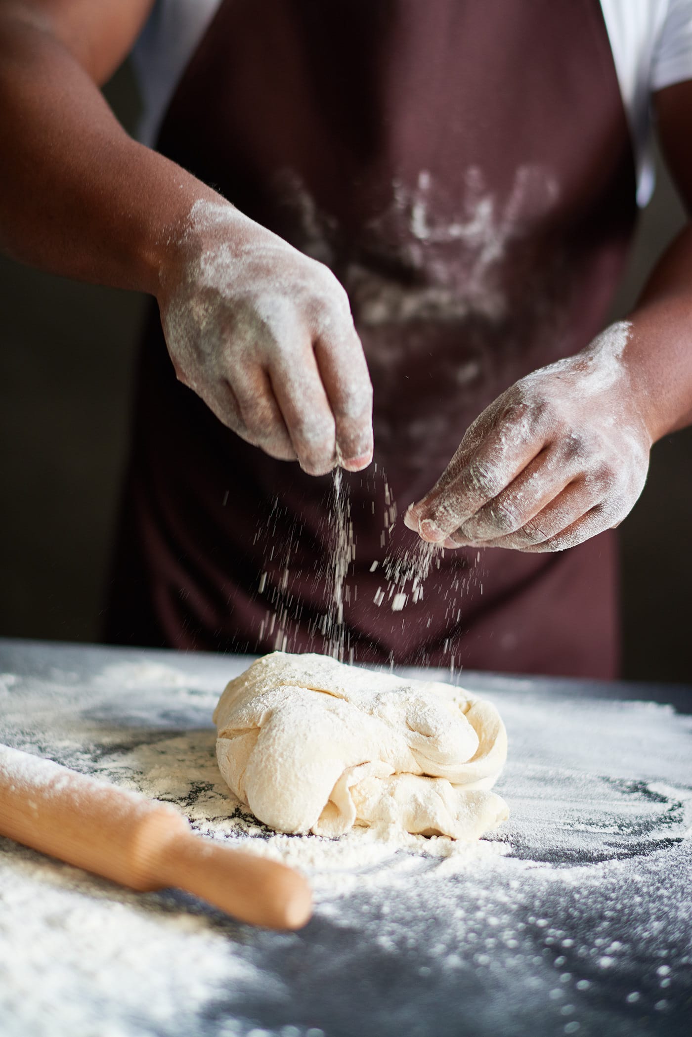 Close-up view of unrecognizable African American cook in apron sprinkling dough with flour while making homemade bread