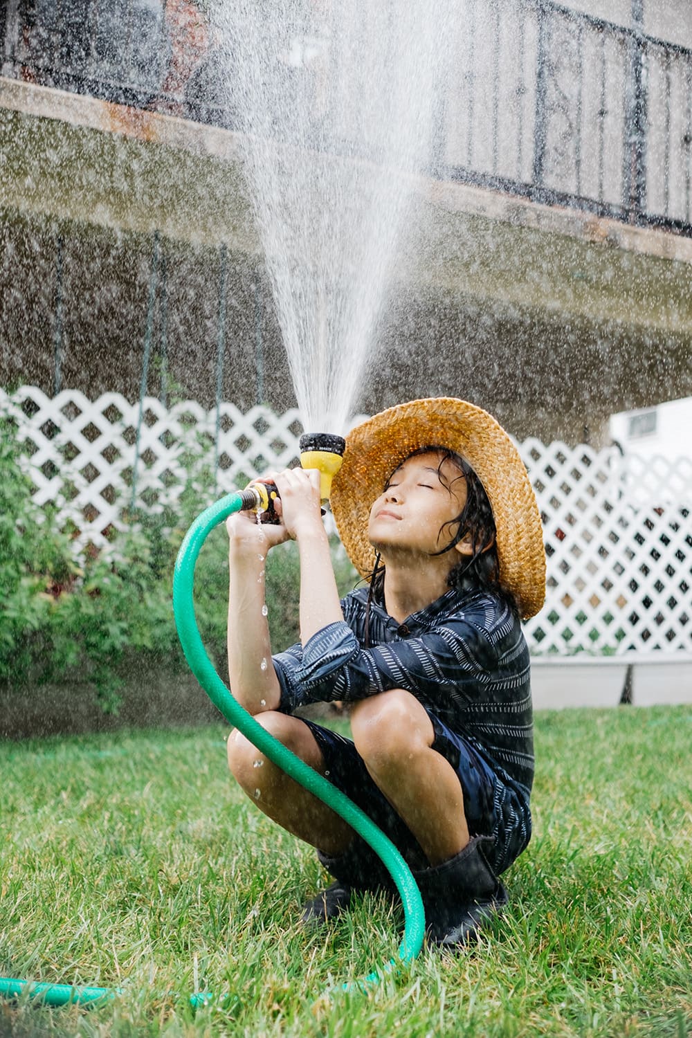 Young Boy Playing With Garden Hose In Backyard