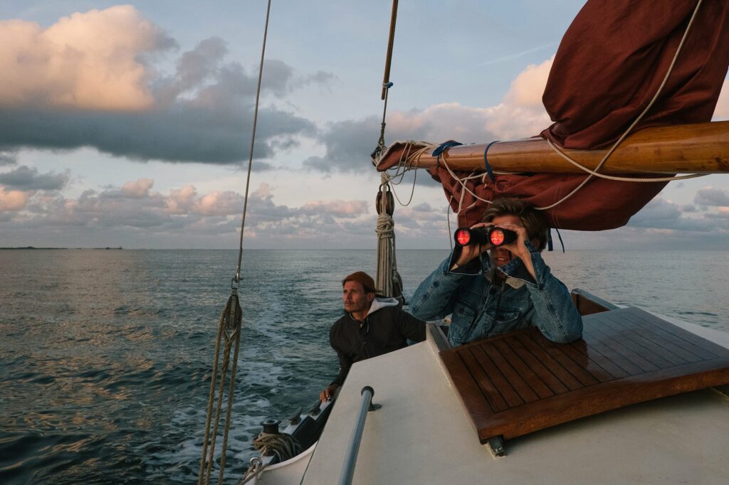 Two Adventurous Sailors On A Sailboat Sailing On An Ocean During Sunset