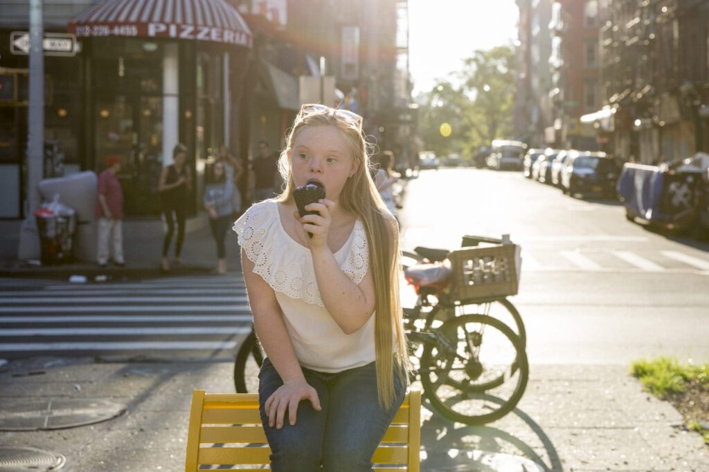 Teenager Eating Ice Cream In An Urban Environment. A young woman with down syndrome eating ice cream