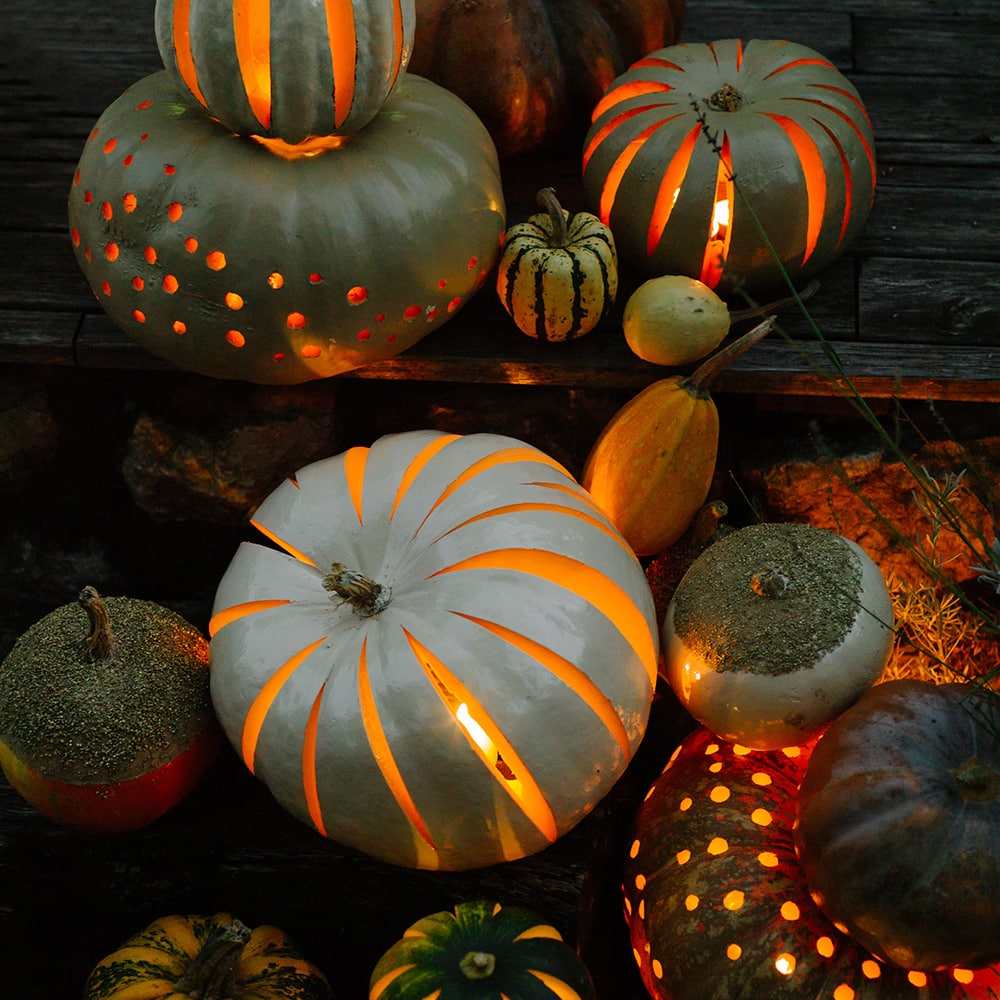 Composition of various pumpkins carved and painted glowing in nighttime.