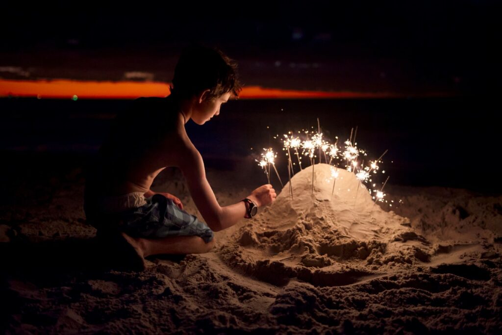 Boy at the beach on a warm summer evening, playing with sparklers after sunset