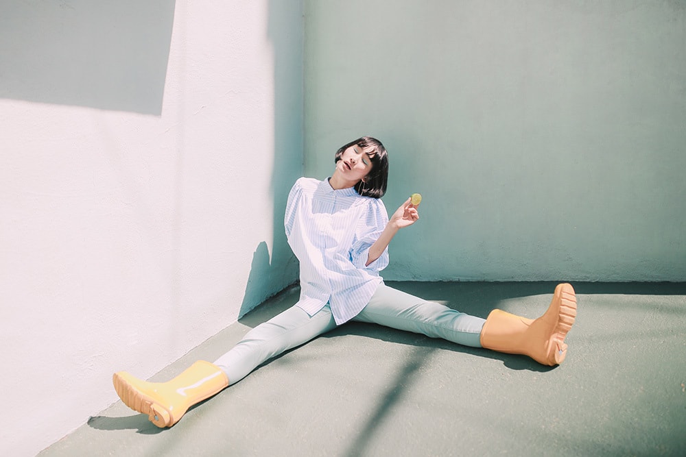 girl lounges in yellow boots and blue clothes by a house with a lime