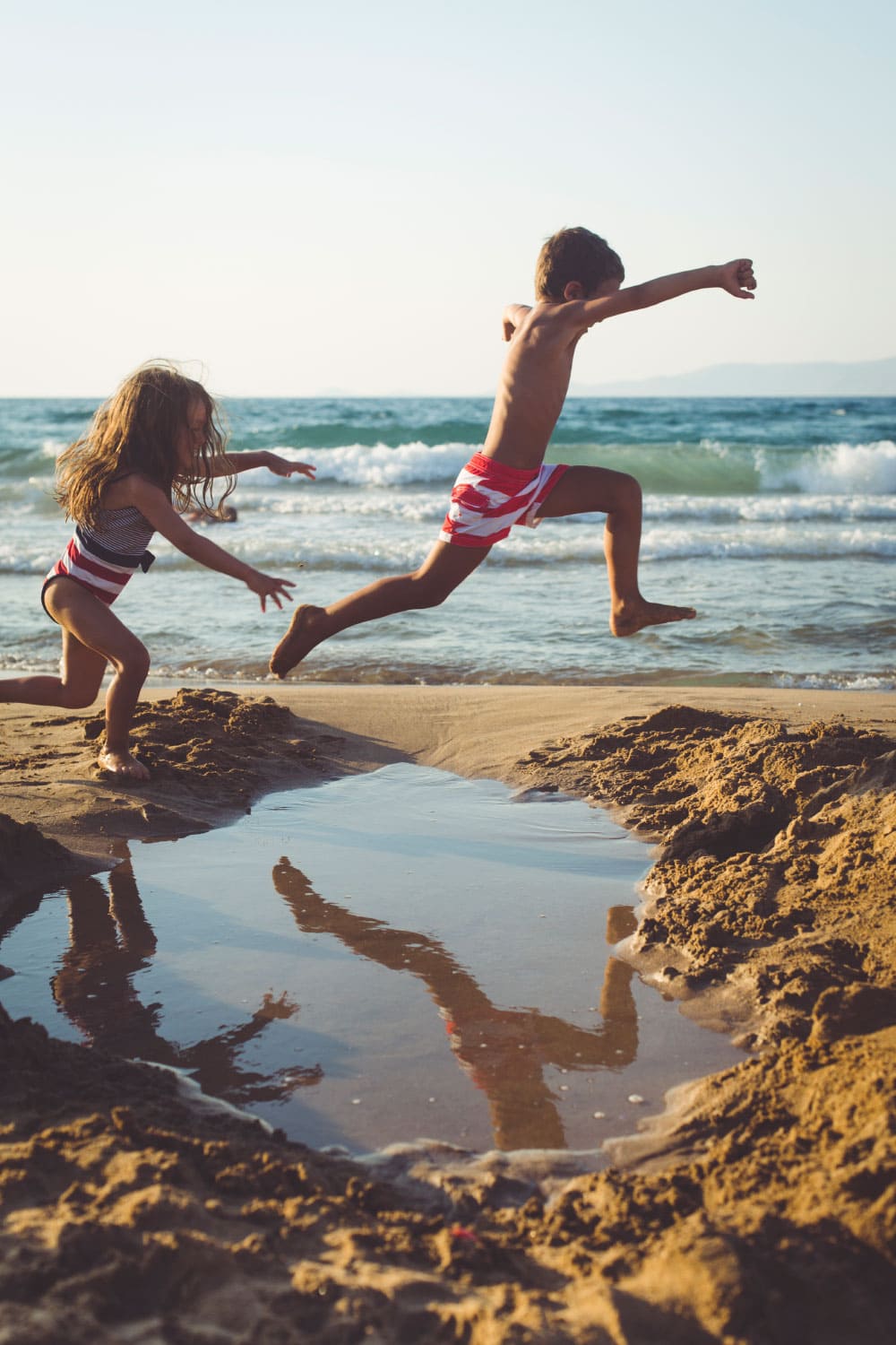 boy and girl jumping in the sand on the beach