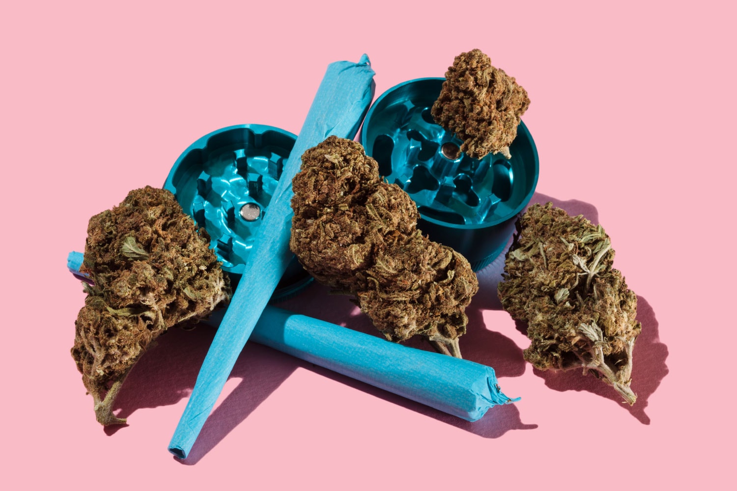 Buds, grinder and joints on pink background.