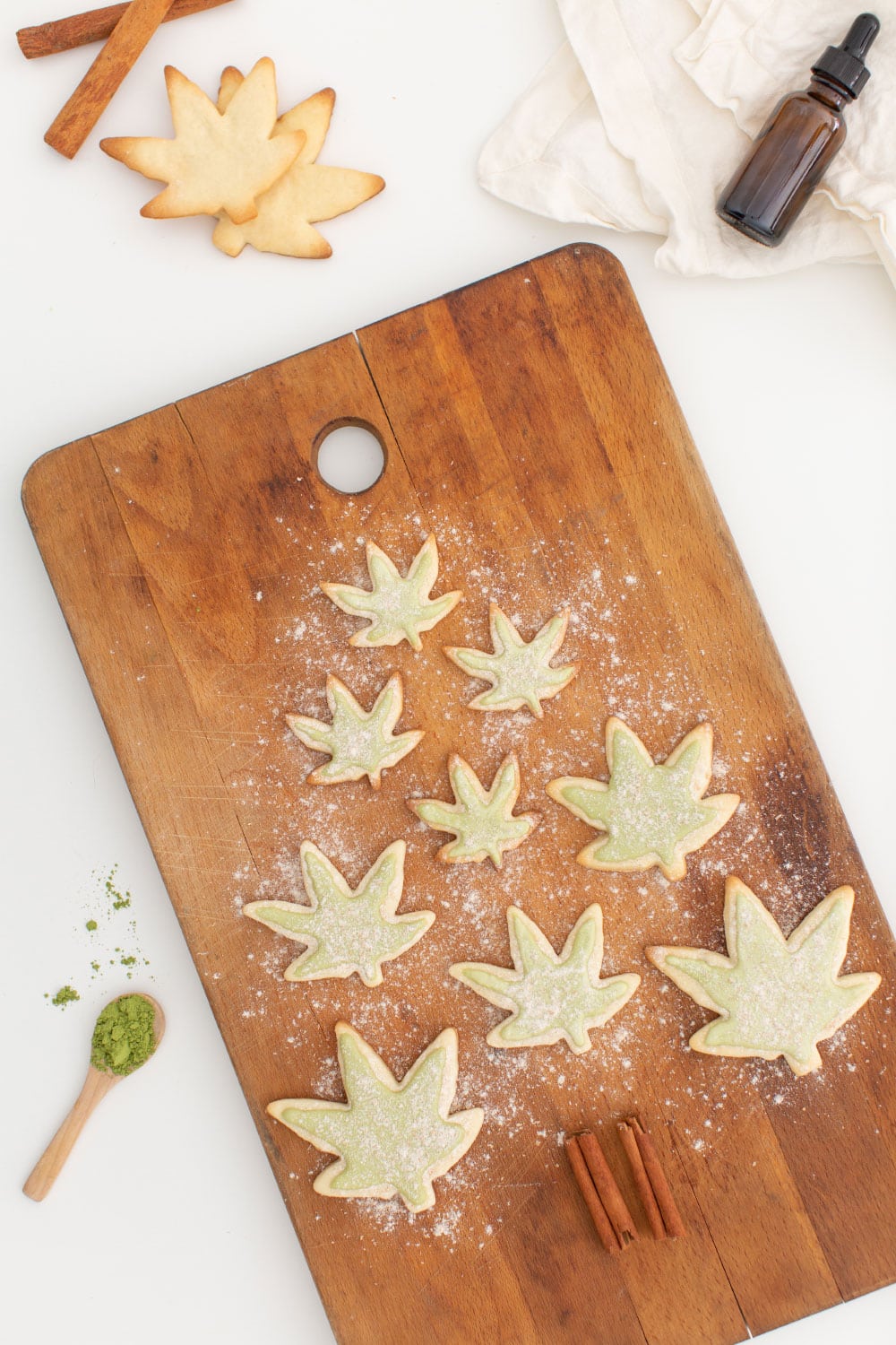 Marijuana pot shaped leaf sugar cookies infused with cbd oil, with green icing from matcha powder and flour on wooden cutting board surface, shaped into a Christmas tree.
