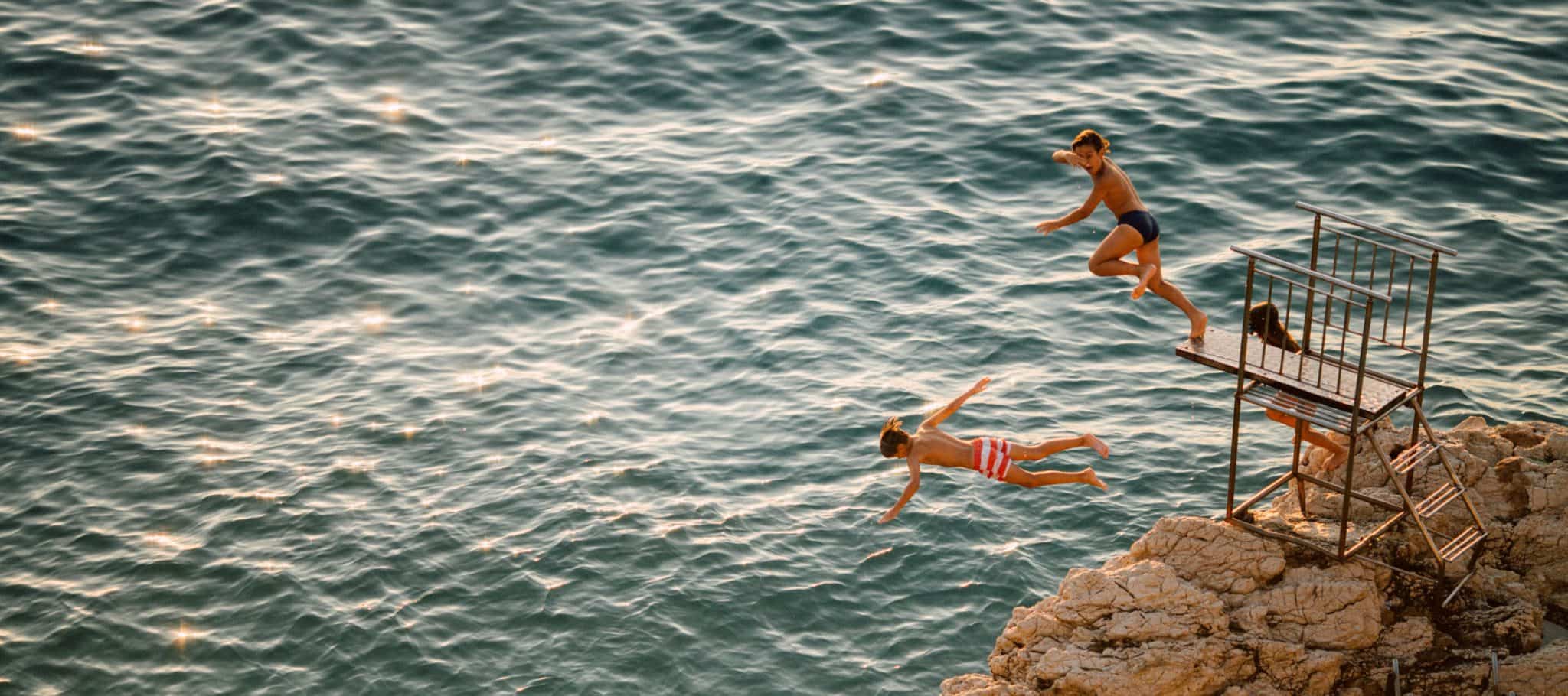 Two children jumping from a cliff.