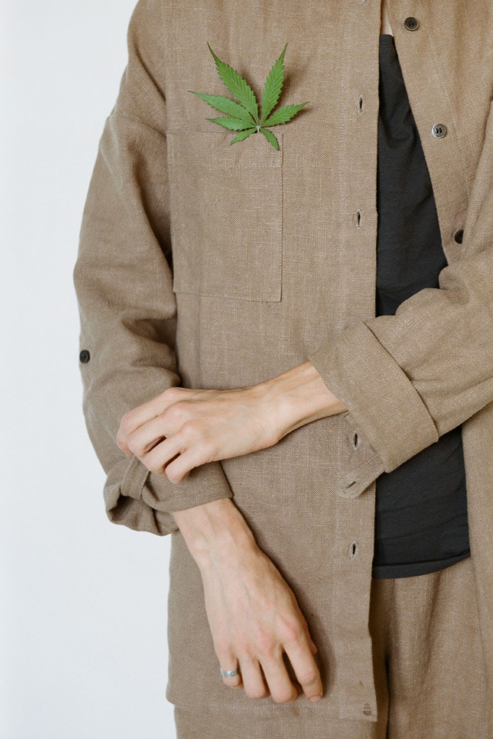 Unrecognizable female in brown hemp shirt scratching arm while standing on white background