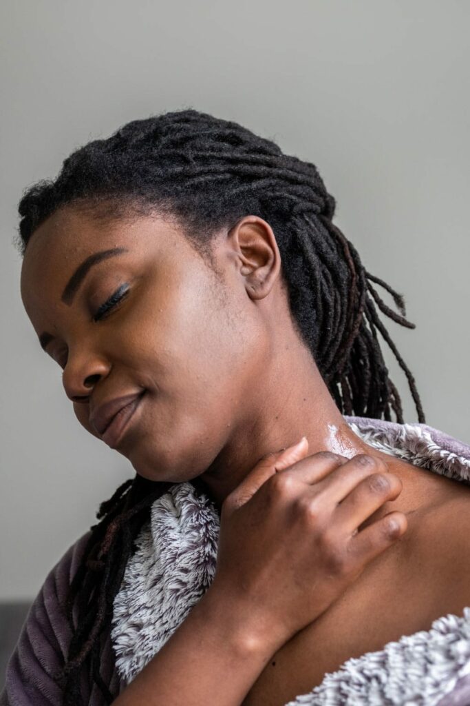 Black woman sitting in her bed applying some CBD Balm onto her skin. CBD also known as Cannabidiol is great for relieving all types of symptoms. The model