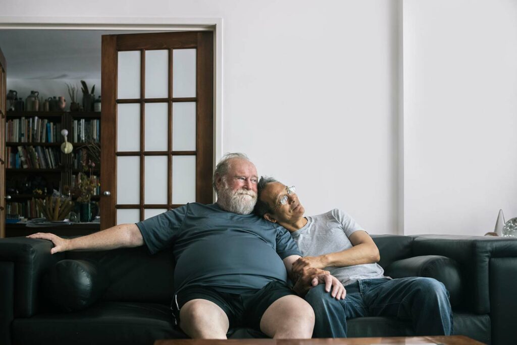 Portrait Of Loving Retired Senior Gay Couple Sitting Together At Home Love springs eternal.