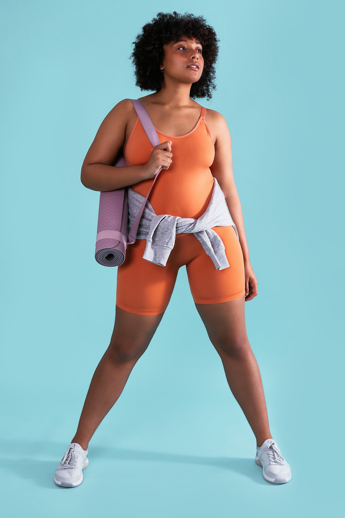 Full body self assured curvy female athlete with mat looking away while standing against blue background during workout