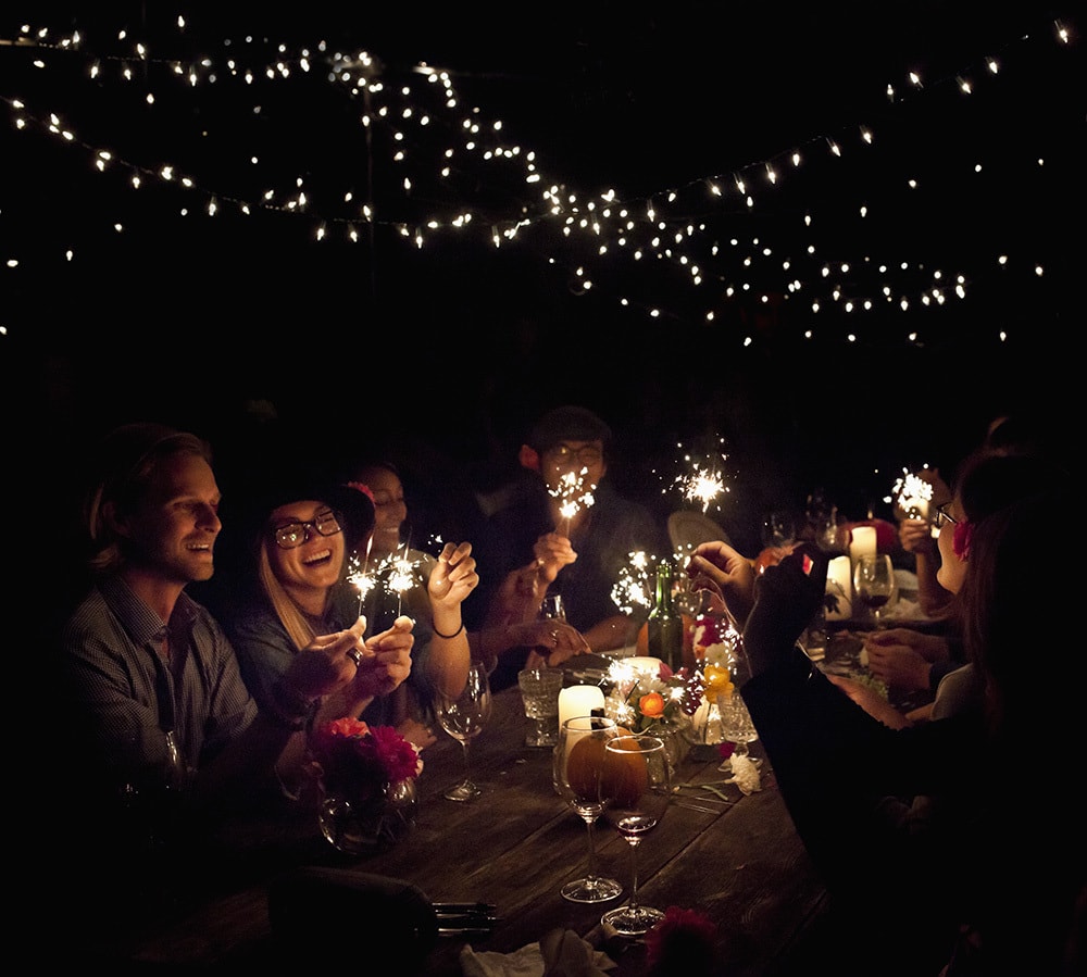 Backyard dinner party with joyful people lighting sparklers.
