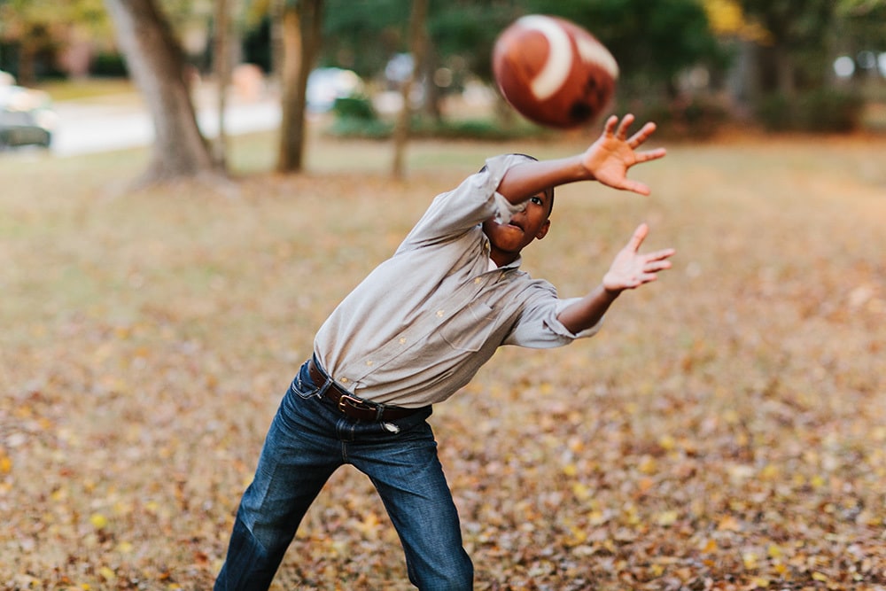 A Young Boy In The Neighborhood Park Playing Catch With A Football