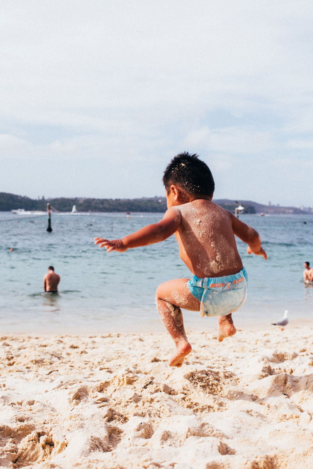 A toddler jumps into the air over a sandy summer beach in beautiful Sydney Australia.