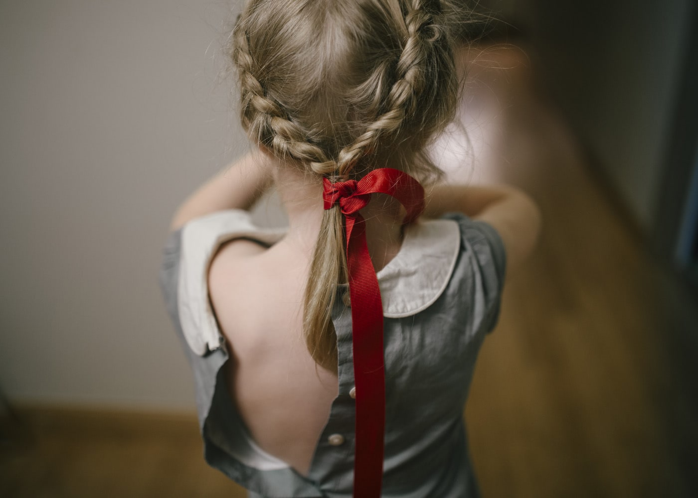 Back View of a little Girl in a red ribbon and braided hair with the back of her vintage dress unbuttoned.