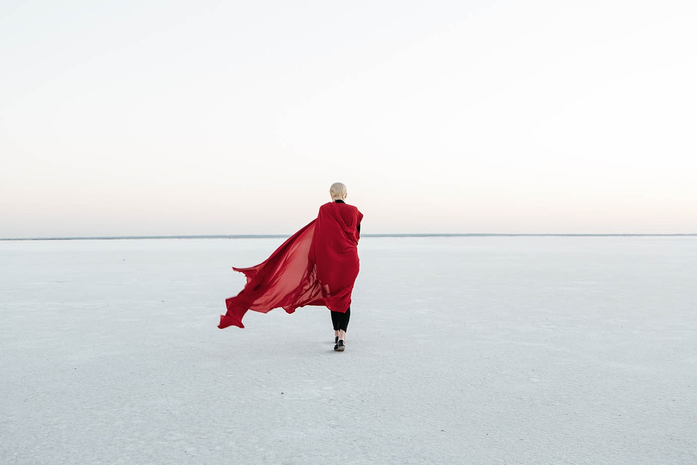 Woman walking through salt flats with fabric wrapped around her and blowing in the wind