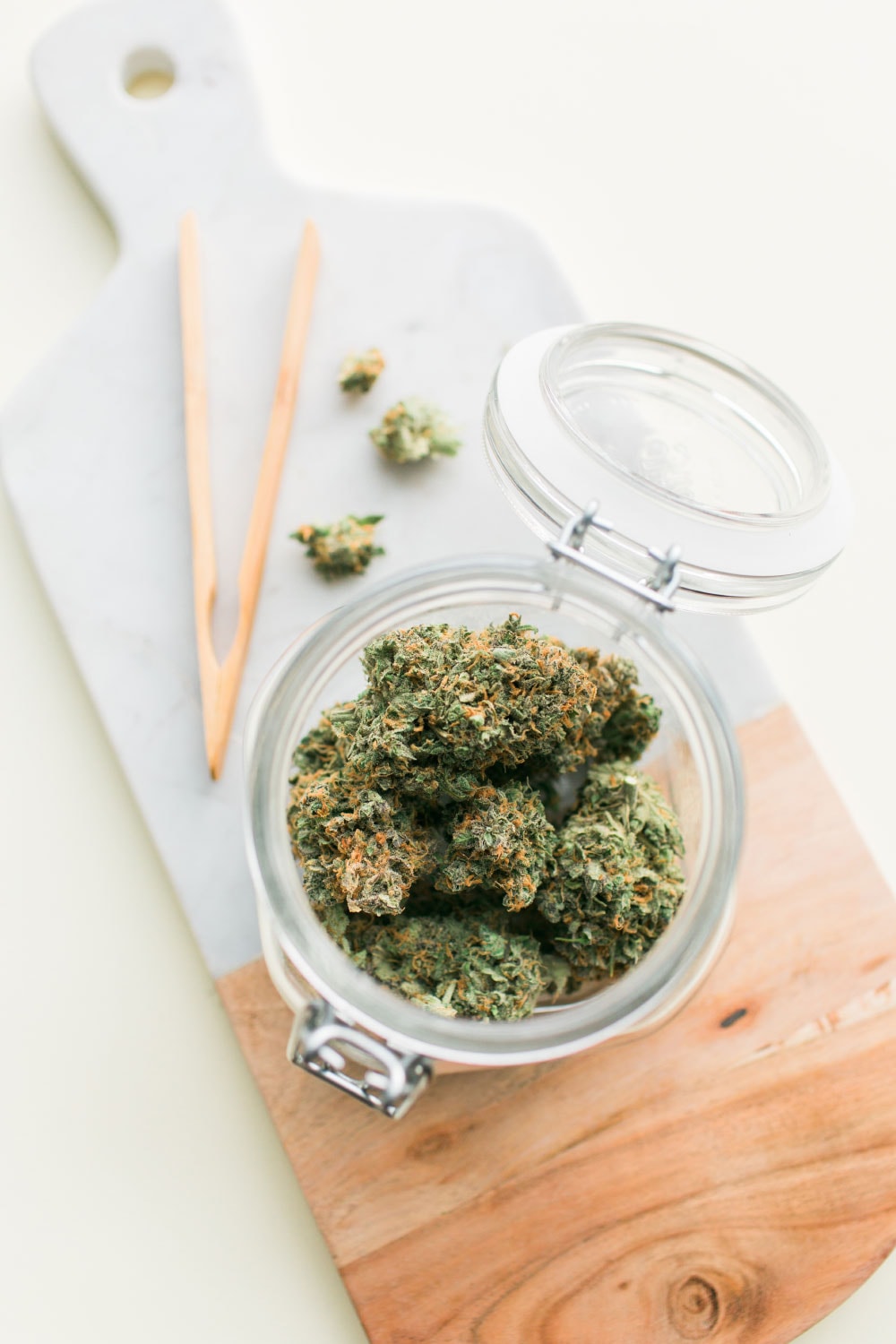 Jar Of Marijuana And Tongs On Cutting Board