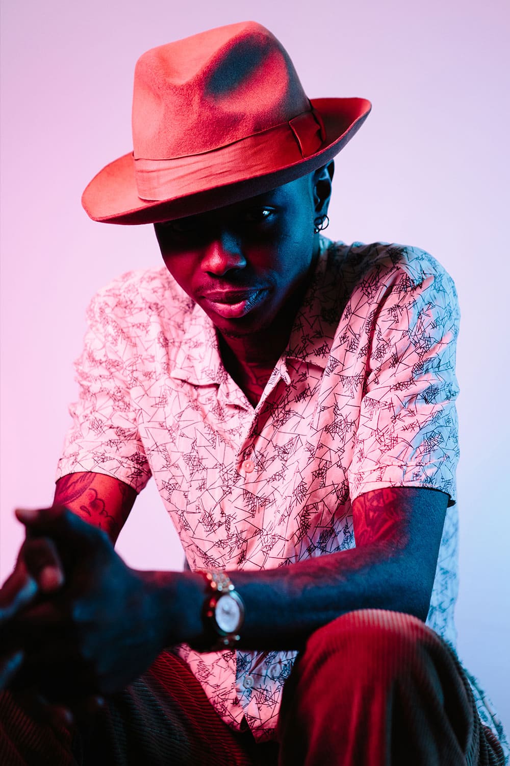 Strongly lit portrait of an elegant tattooed black man in short sleeved shirt and hat