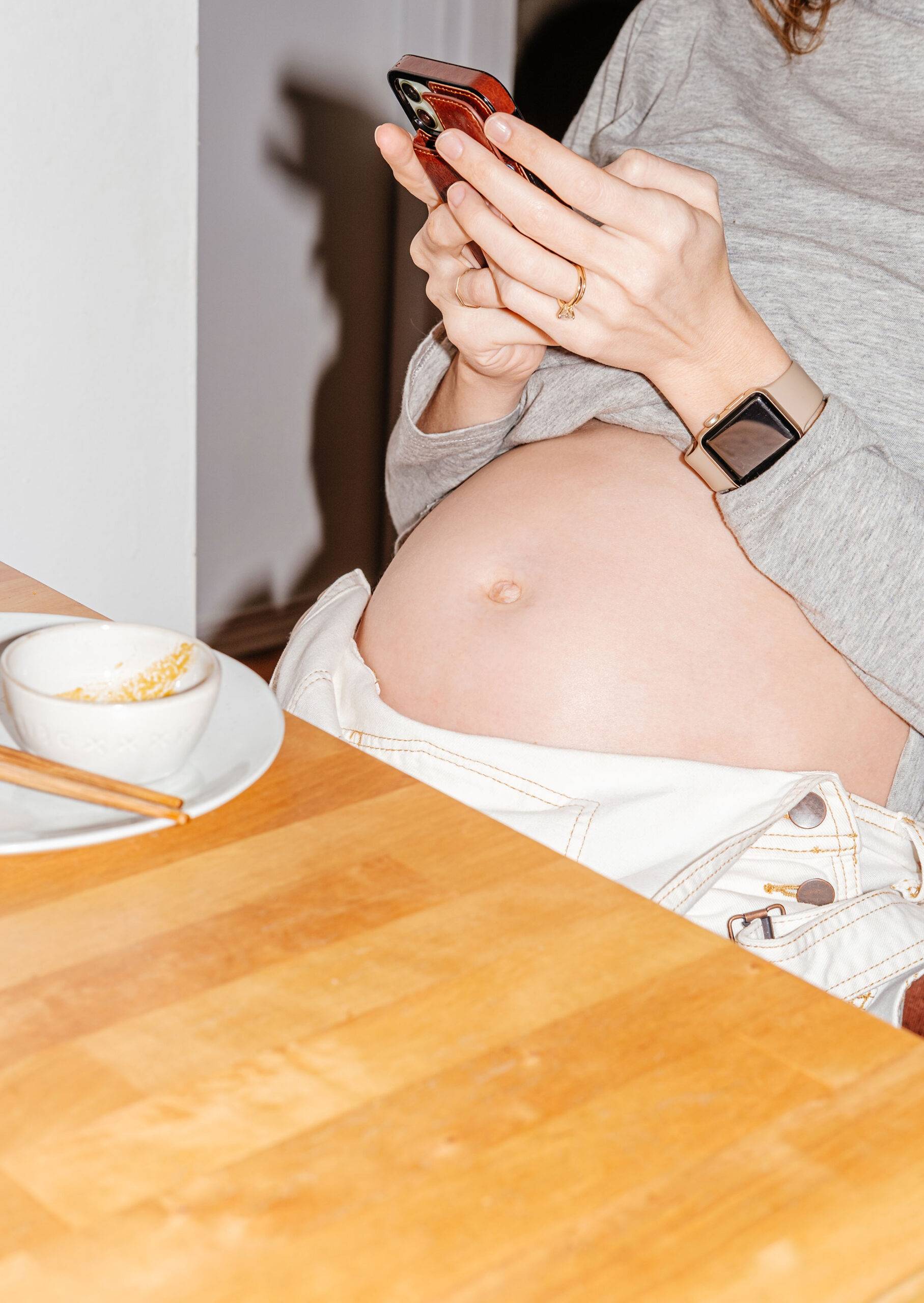 Pregnant woman sitting at a table with pregnant belly exposed after eating a meal. Expectant mother with a pregnancy belly.