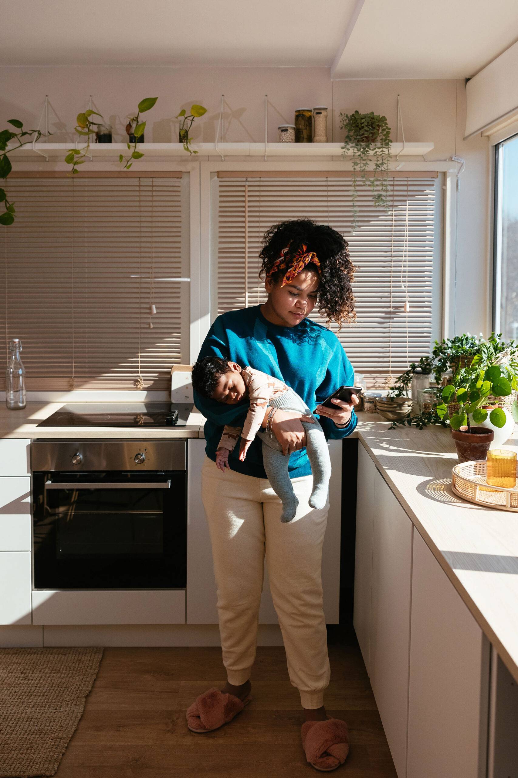 Mom With Baby Using Smartphone In Kitchen