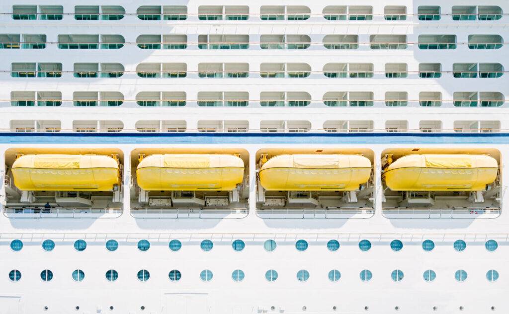 Many layers of cabins and port holes and lifeboats on the side of large cruise ship