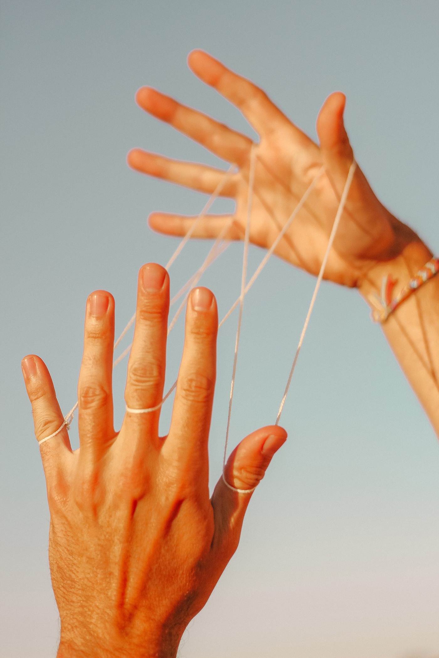 Non-gender specific hands playing cat's cradle against sky