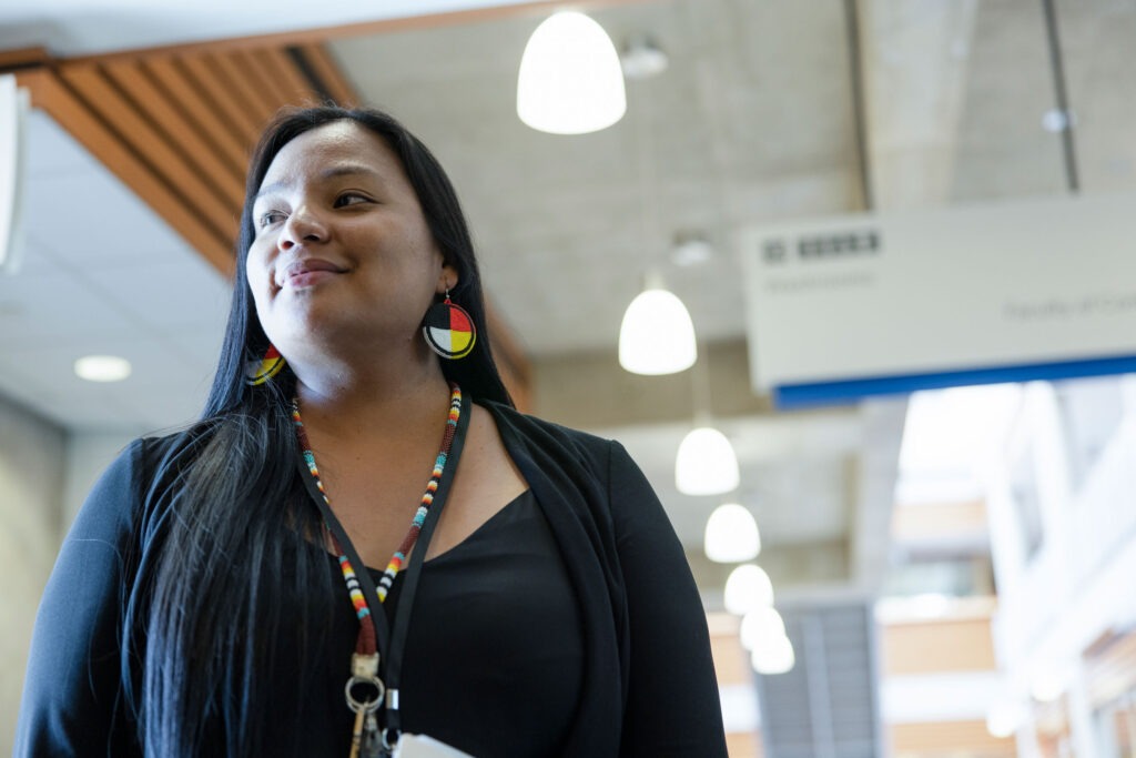 Portrait of confident Indigenous woman in office setting looking away from camera. She is wearing traditional styled beaded jewelry