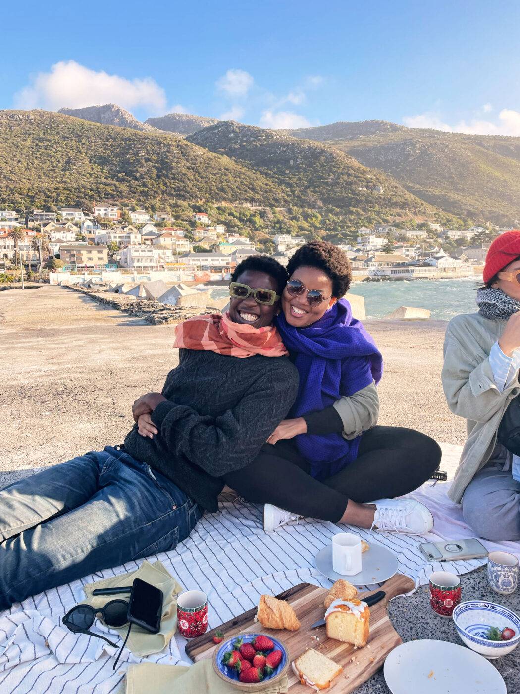 Happy friends smile for a group portrait while on summer vacation having a picnic outside on a harbour wall in summer