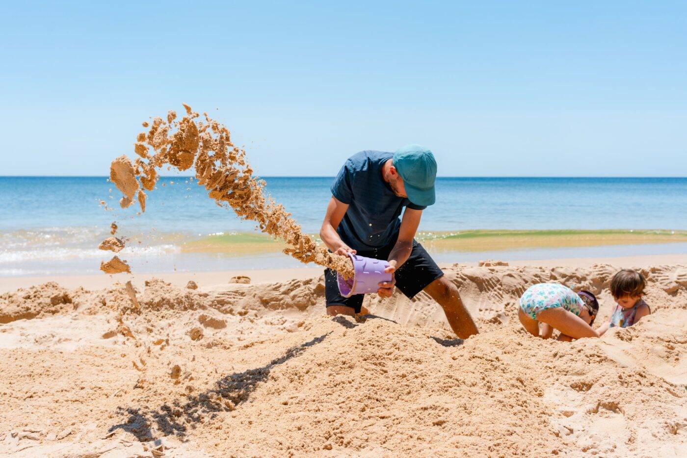 Family beach summer vacation day. Father and two young daughters making a sandcastle on the beach in Portugal.