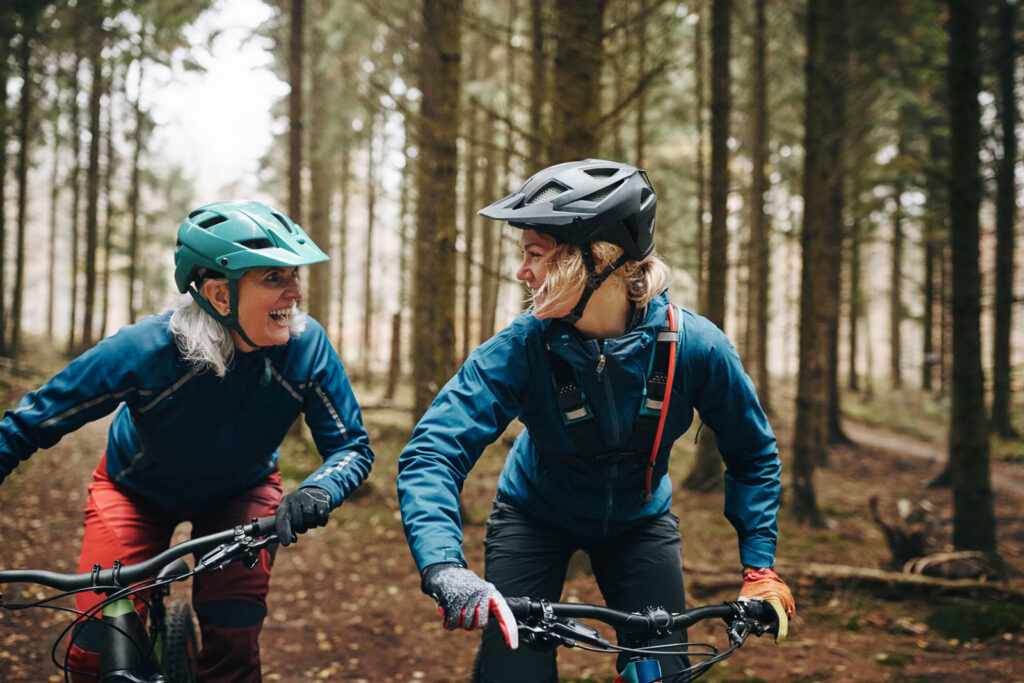 Smiling mother and daughter riding mountain bikes together along a trail in a misty forest