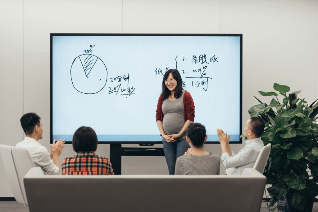 Young Asian pregnant woman giving presentation to a group of business people with office screen