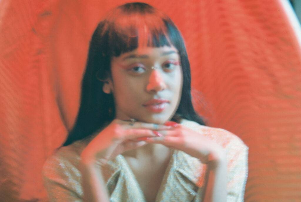 Female Gaze Young woman with long hair and cropped bangs poses to camera in front of a red drape, soft focus film look