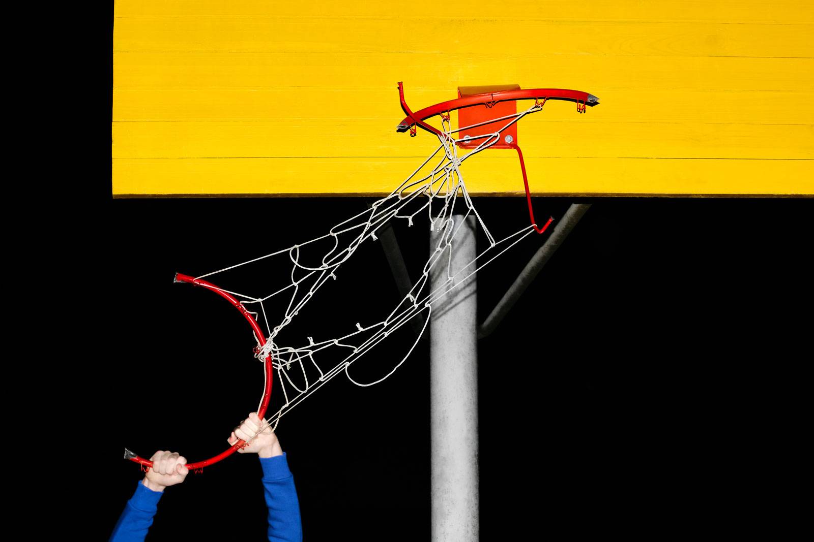 Hands holding a broken basketball hoop at night. Bad game. Hooliganism. The combination of yellow red and blue on a dark background