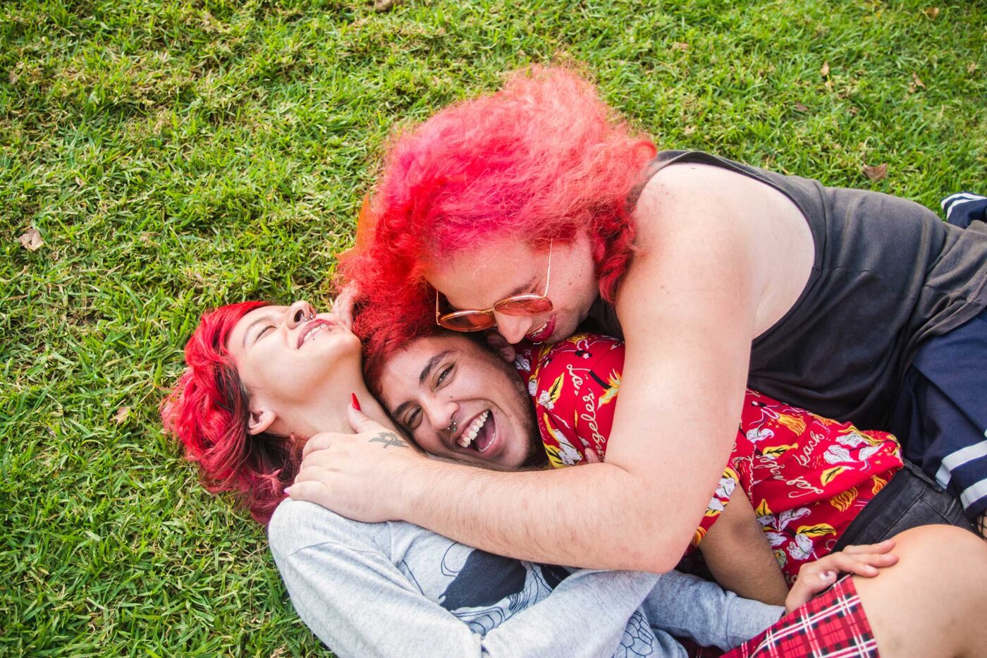 Three latino transgender friends are lying in the grass in a park hugging each other lovingly and having fun. LGBTQ friendship and community.