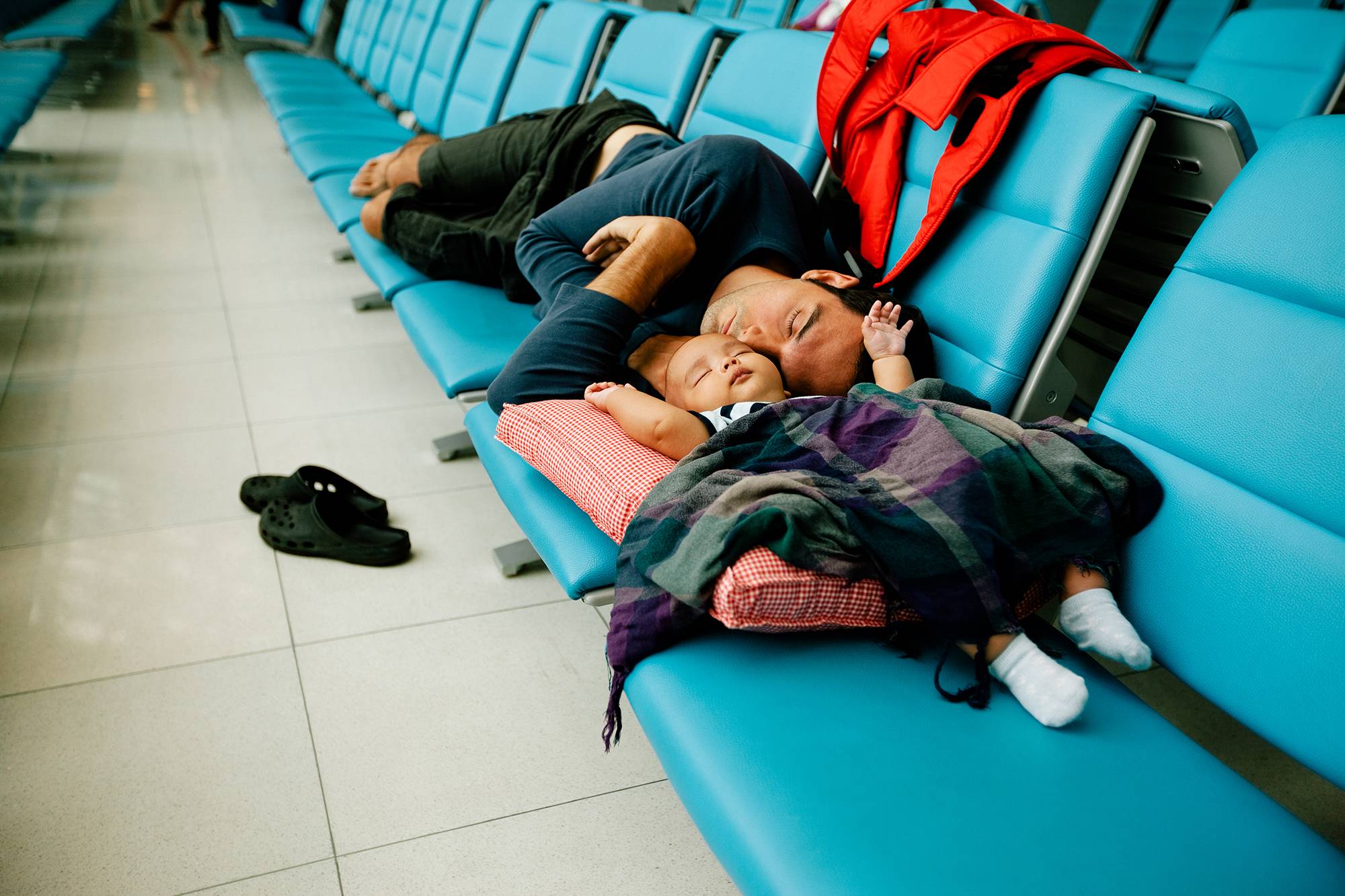 Cute baby and young father sleeping on the seats while waiting for the next flight at the airport.