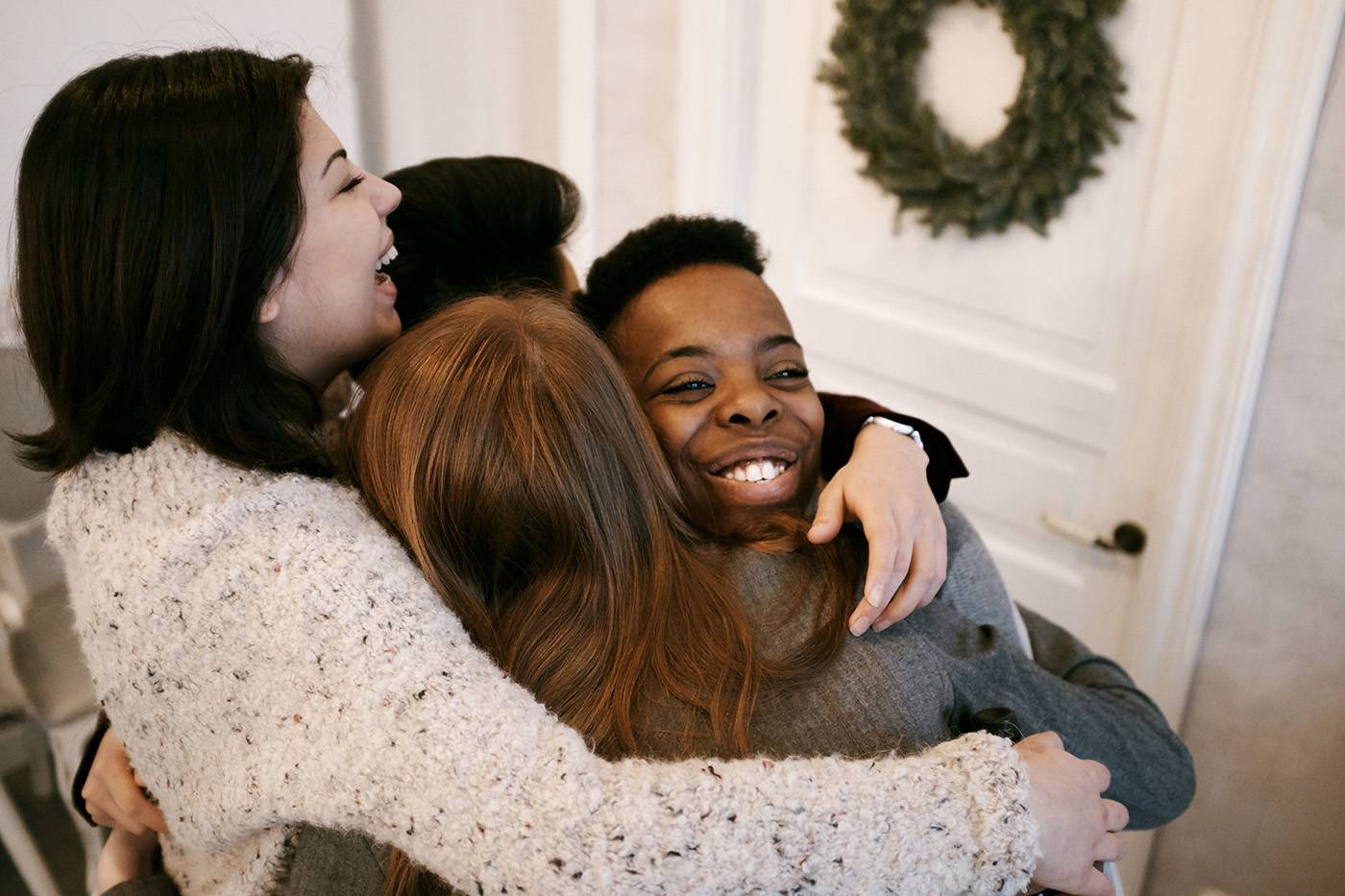 Multiethnic group of young women hugging each other and smiling happily while having Christmas party at home