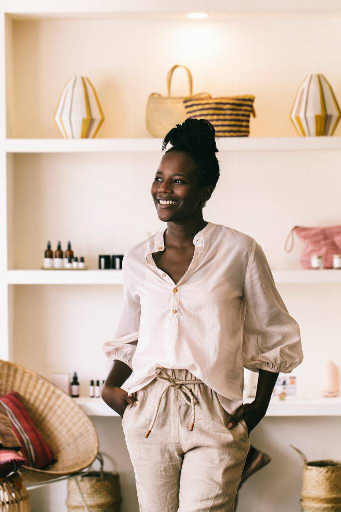 Environmental indoor portrait of a smiling young african woman standing in a small boutique. She is wearing a organic clothing and is looking away.