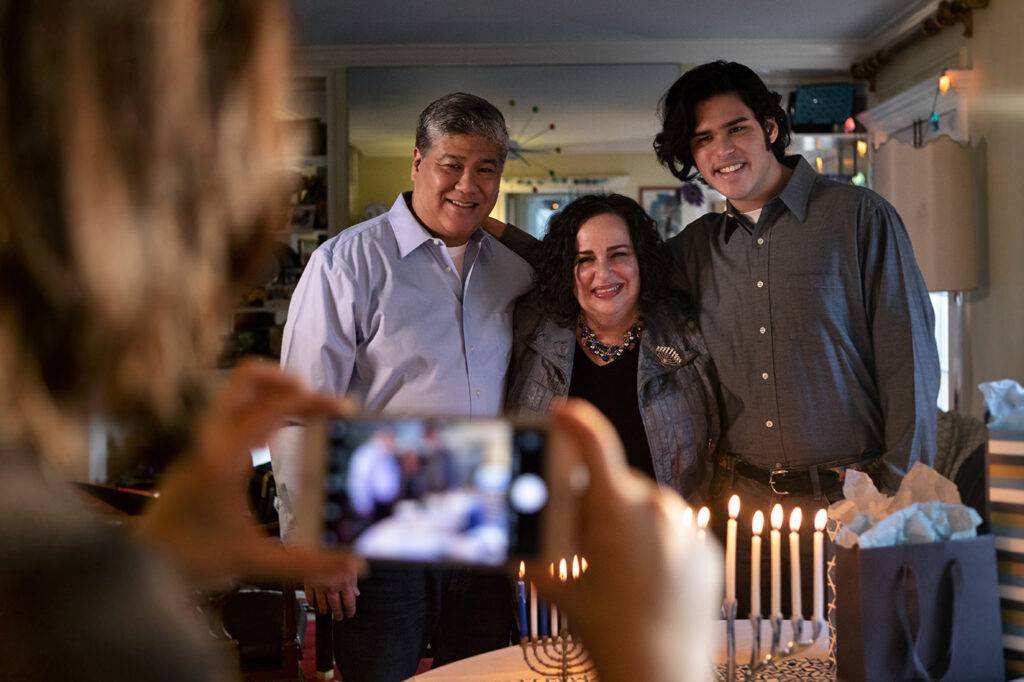 Nuclear family celebrates the Jewish holiday of Hanukkah at home, with menorah candle lighting and playing dreidel.