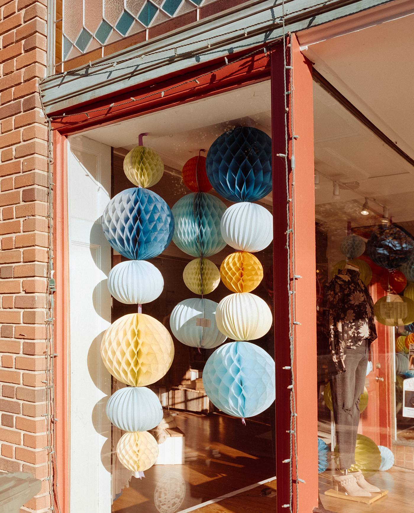 A medium format color film photo of hanging paper globes in a shop showcase window in the bright early morning light.