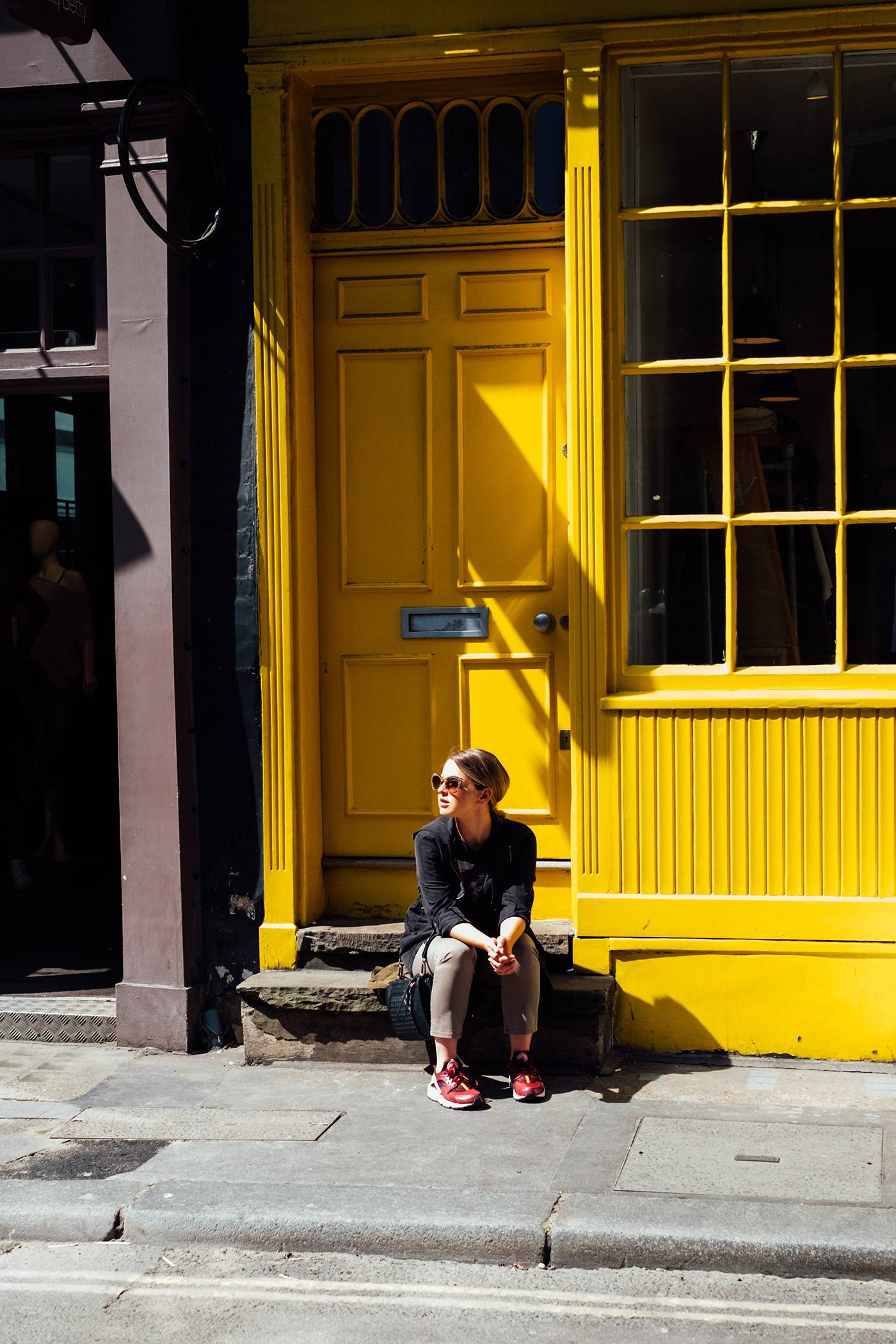 Young Woman Sitting on the Street in Front of the Bright Yellow Shop