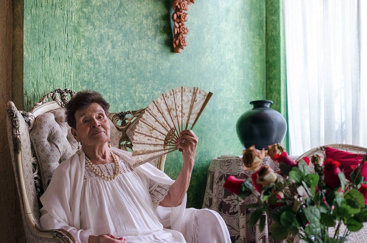 Stylish Mexican old lady with a fan in her house full of antique things
