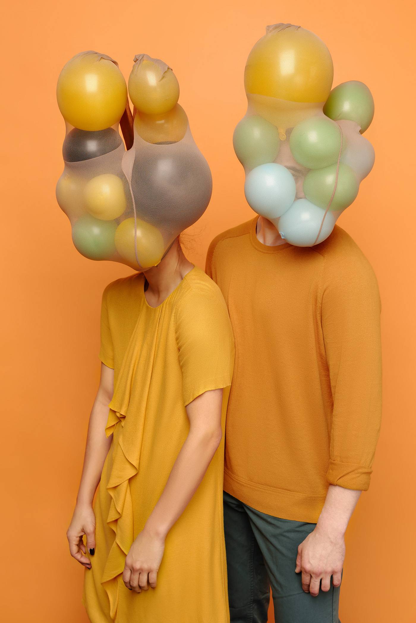 Conceptual photo of unrecognizable couple with balloons in nylon tights instead of their heads standing on orange background